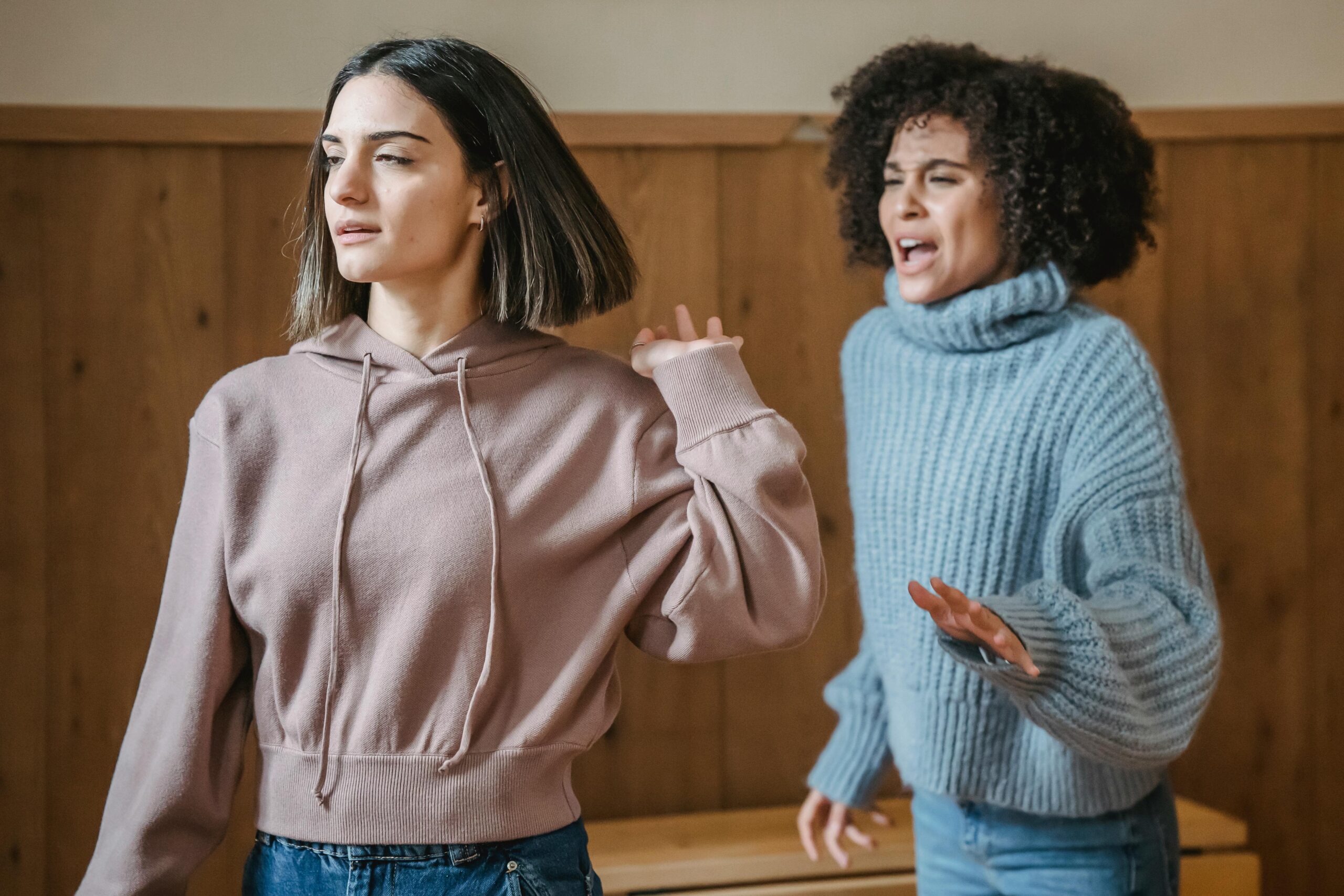 A young woman in a pinkish sweatshirt seems to be showing a challenging behaviour to another woman who looks like she's trying to help her.