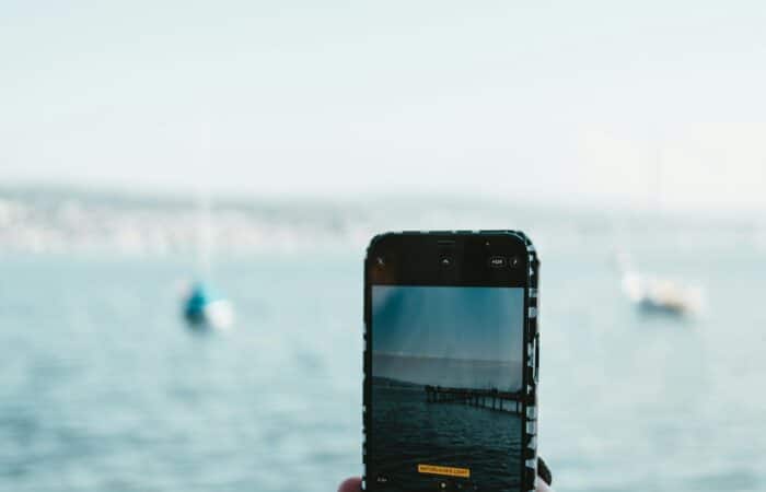 A woman takes a portrait mobile photo of a dock on a lake. There are two boats in the water ahead of her.