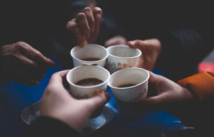 Four people in a circle holding paper coffee cups together.