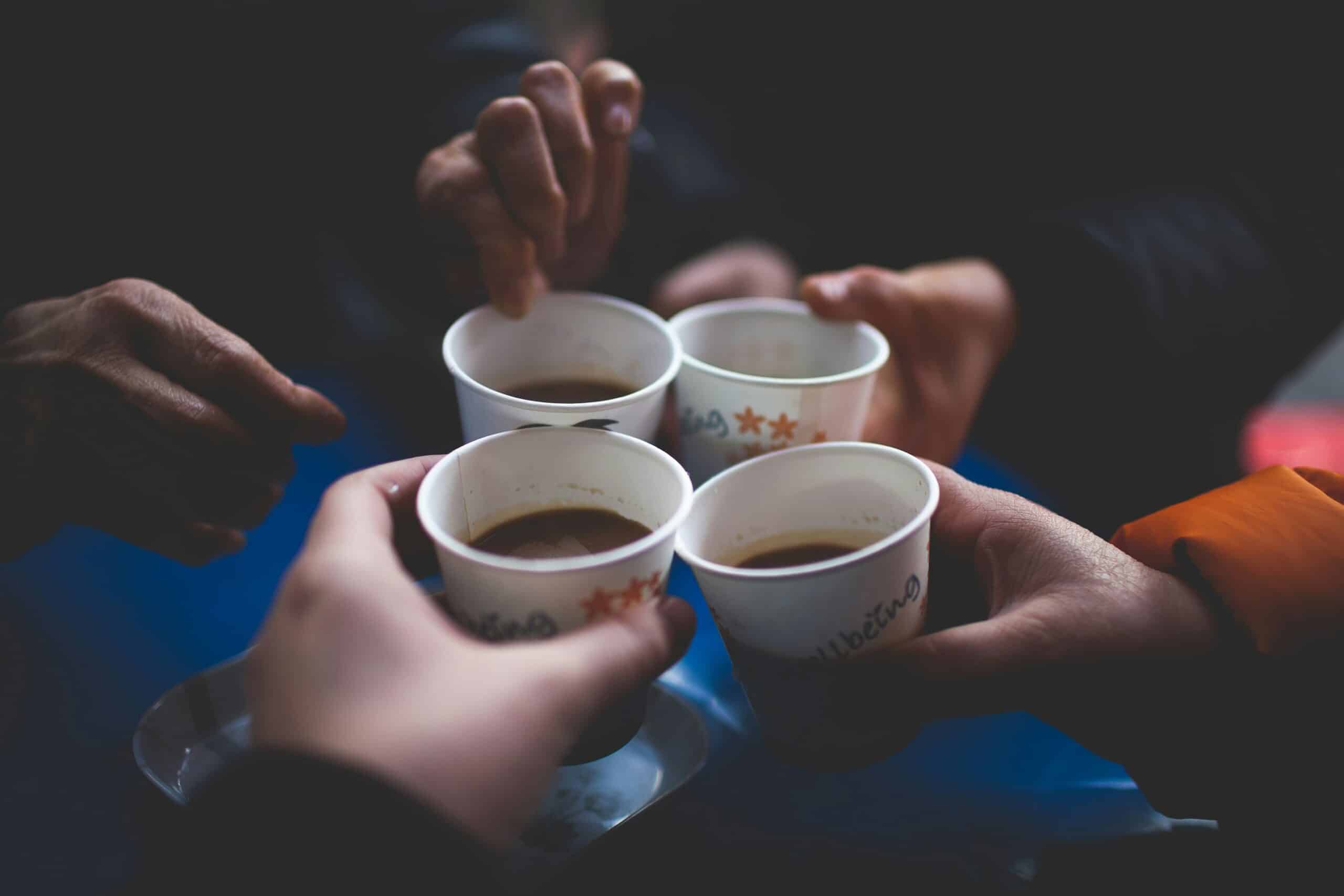 Four people in a circle holding paper coffee cups together.