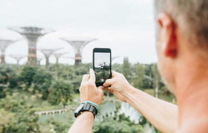 Man takes a picture of futuristic buildings with his mobile phone while standing in greenery.