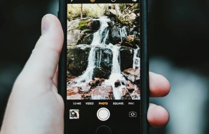 A man takes a photograph of a small waterfall using his mobile phone.