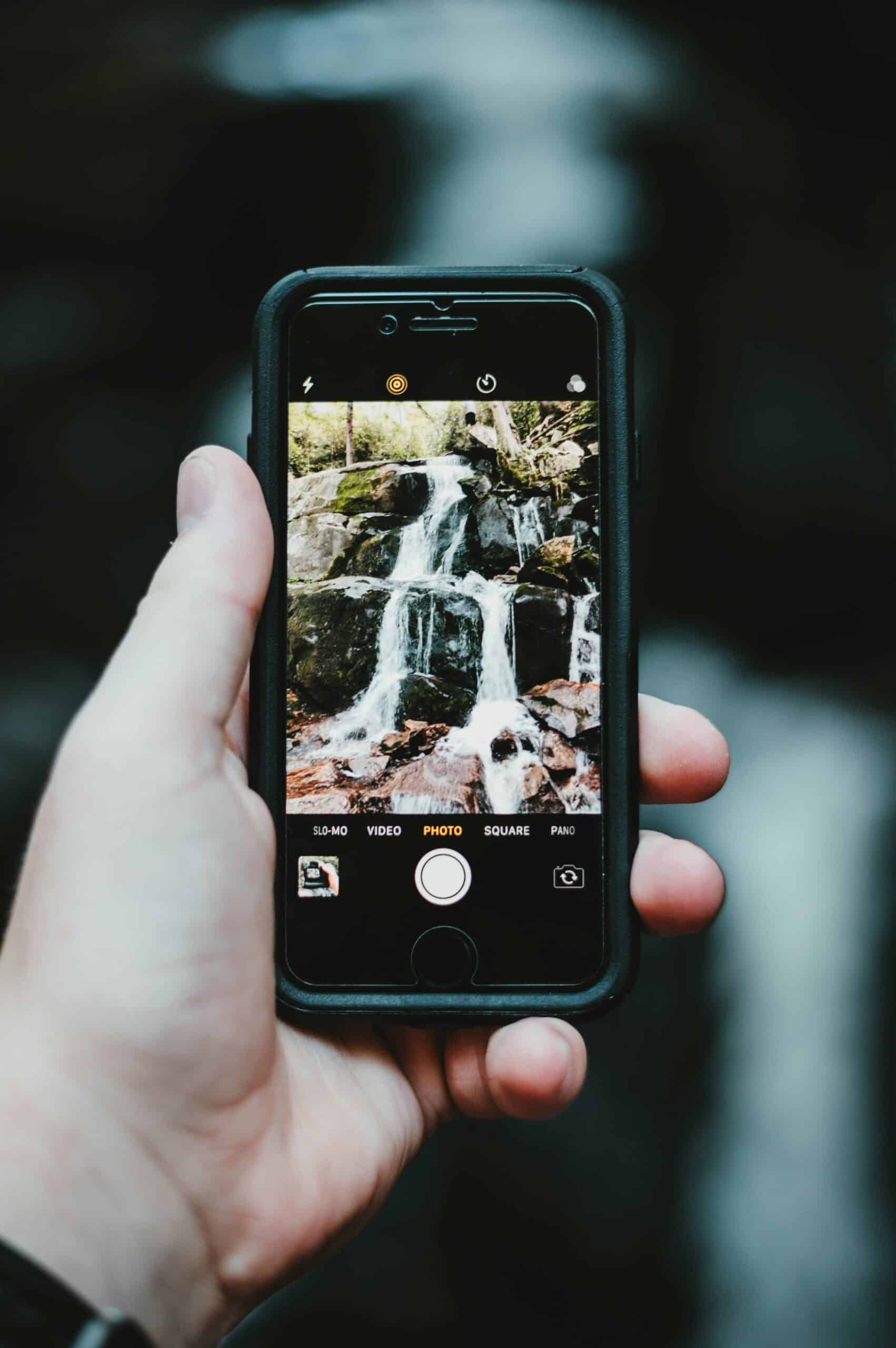 A man takes a photograph of a small waterfall using his mobile phone.