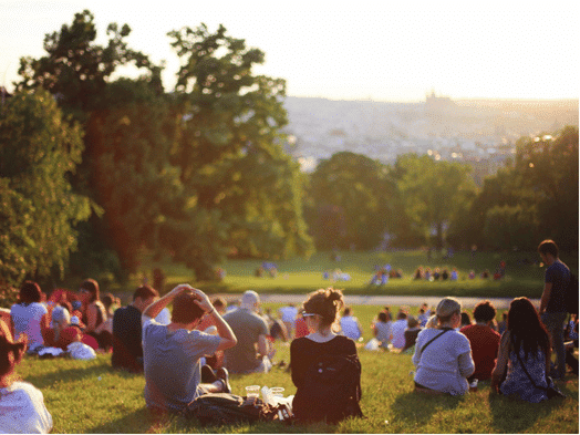 A crowd of people sit on a hill looking at the view of a city