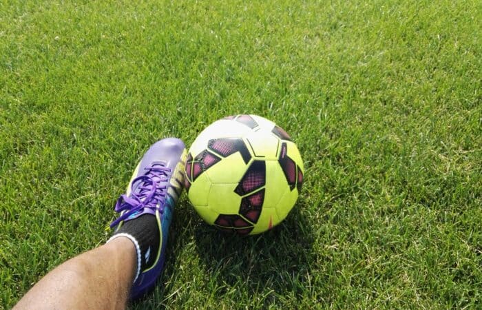 a person wearing a purple football boot touching a yellow and black ball on grass