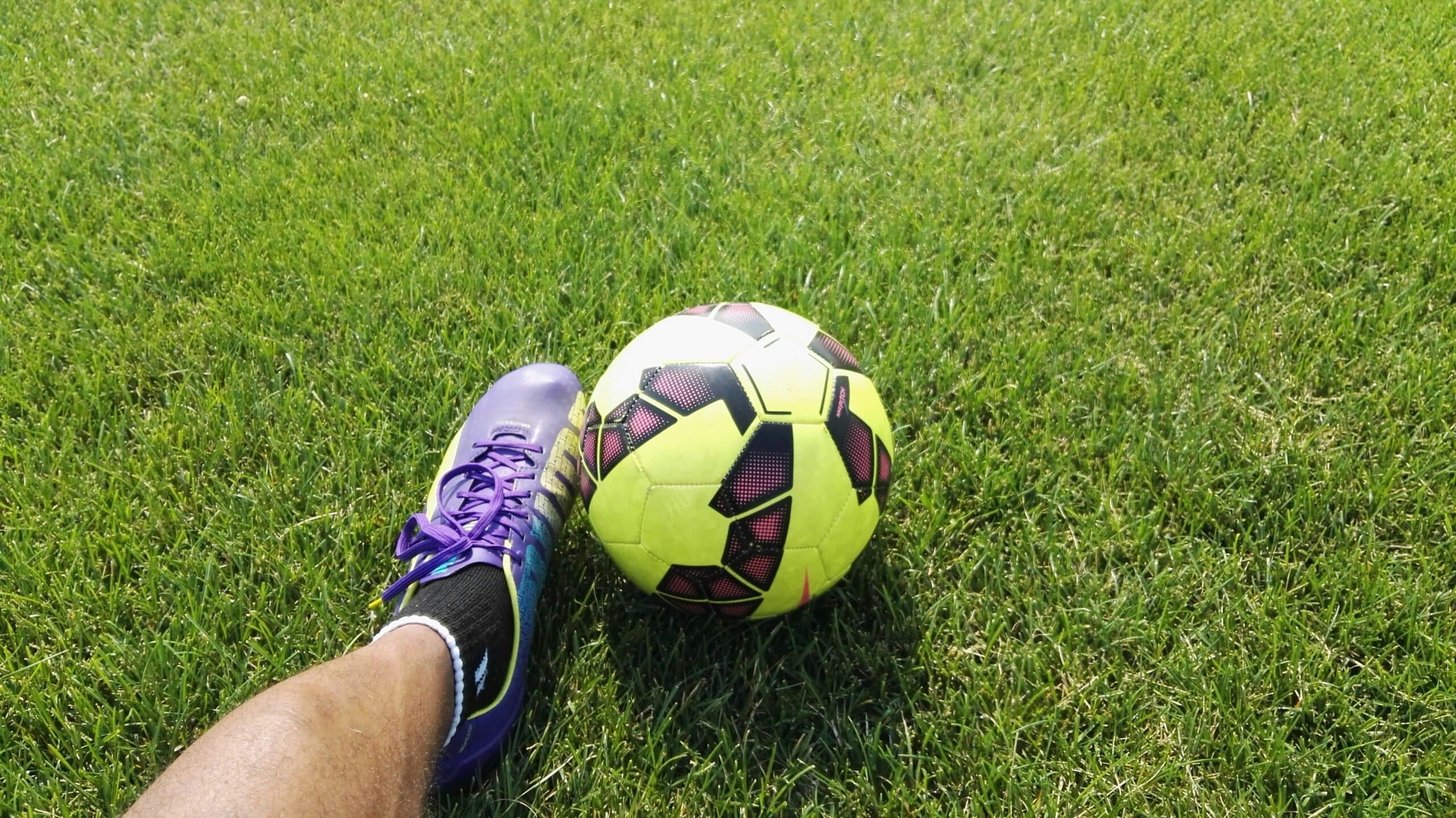 a person wearing a purple football boot touching a yellow and black ball on grass