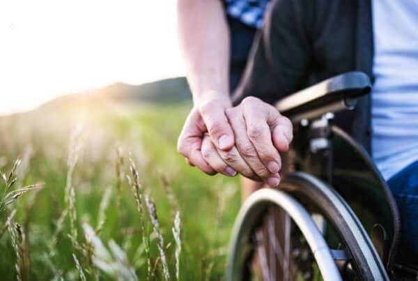 Carer supporting a person in a wheelchair in a grassy field.